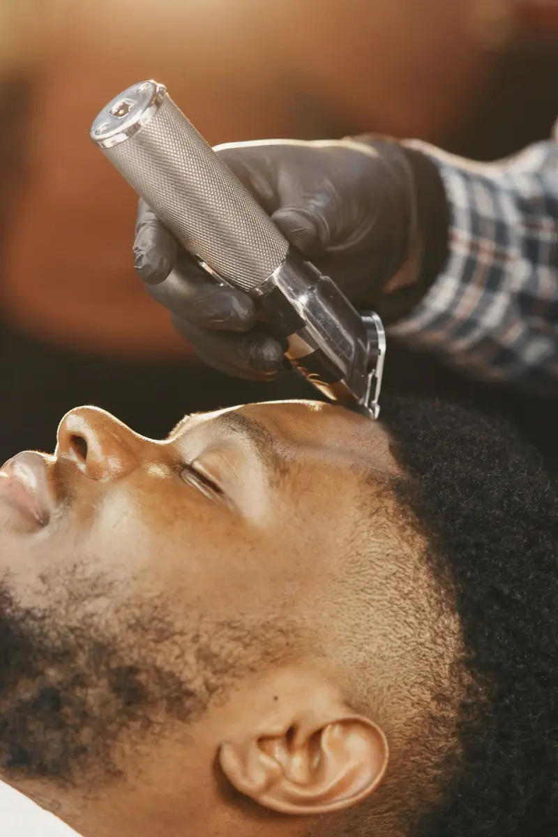 Barber trimming a man's hairline and beard with a clipper