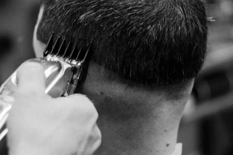 Black and white close-up of a barber's clippers trimming a client's hair