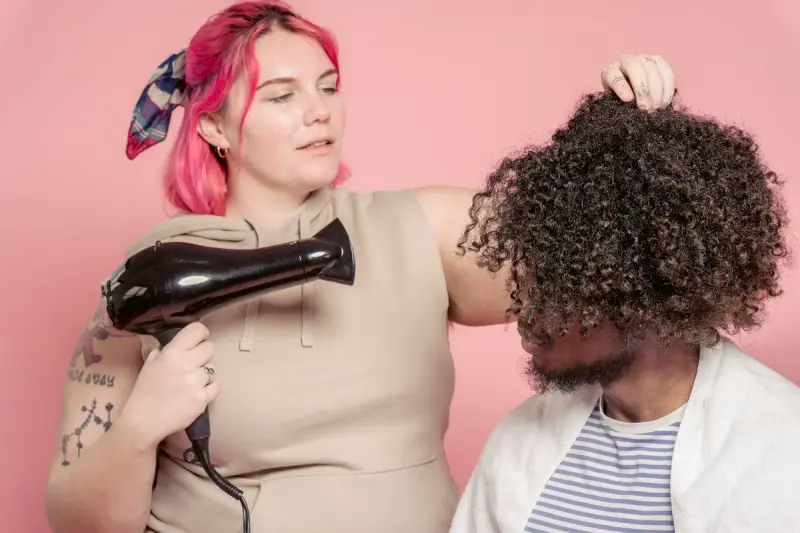 Hairdresser styling a man's curly hair with a hair dryer in a studio