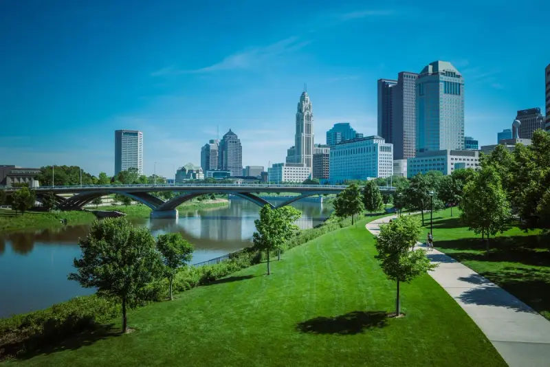 Downtown Columbus skyline above a riverside park on a sunny day