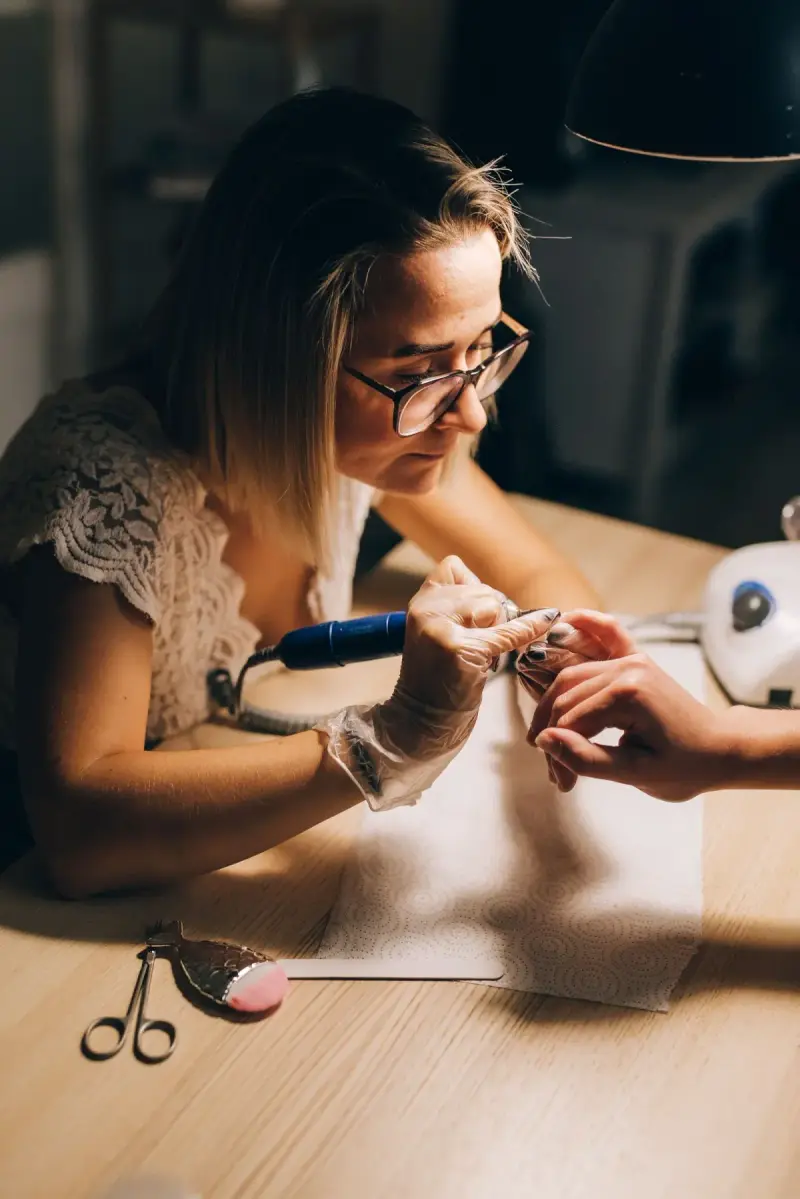 Woman nail technician using a manicure tool at her workstation