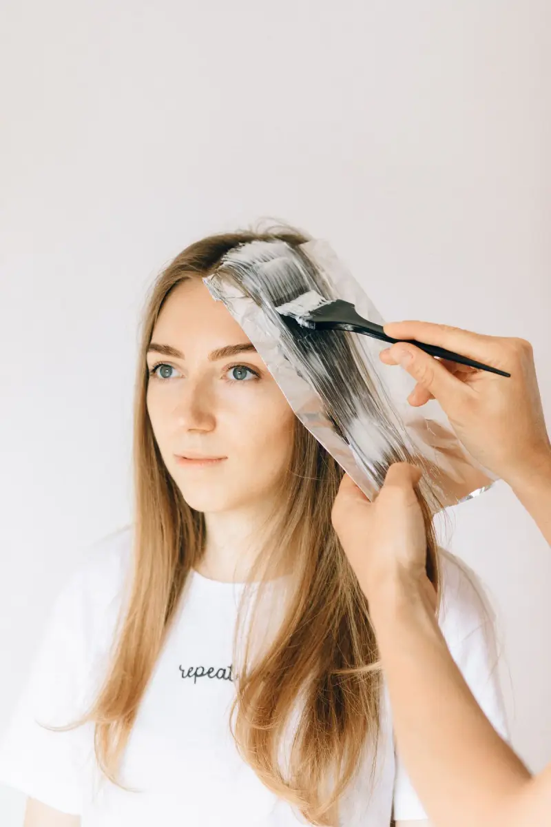 Colorist painting lightener onto a section of long hair over foil