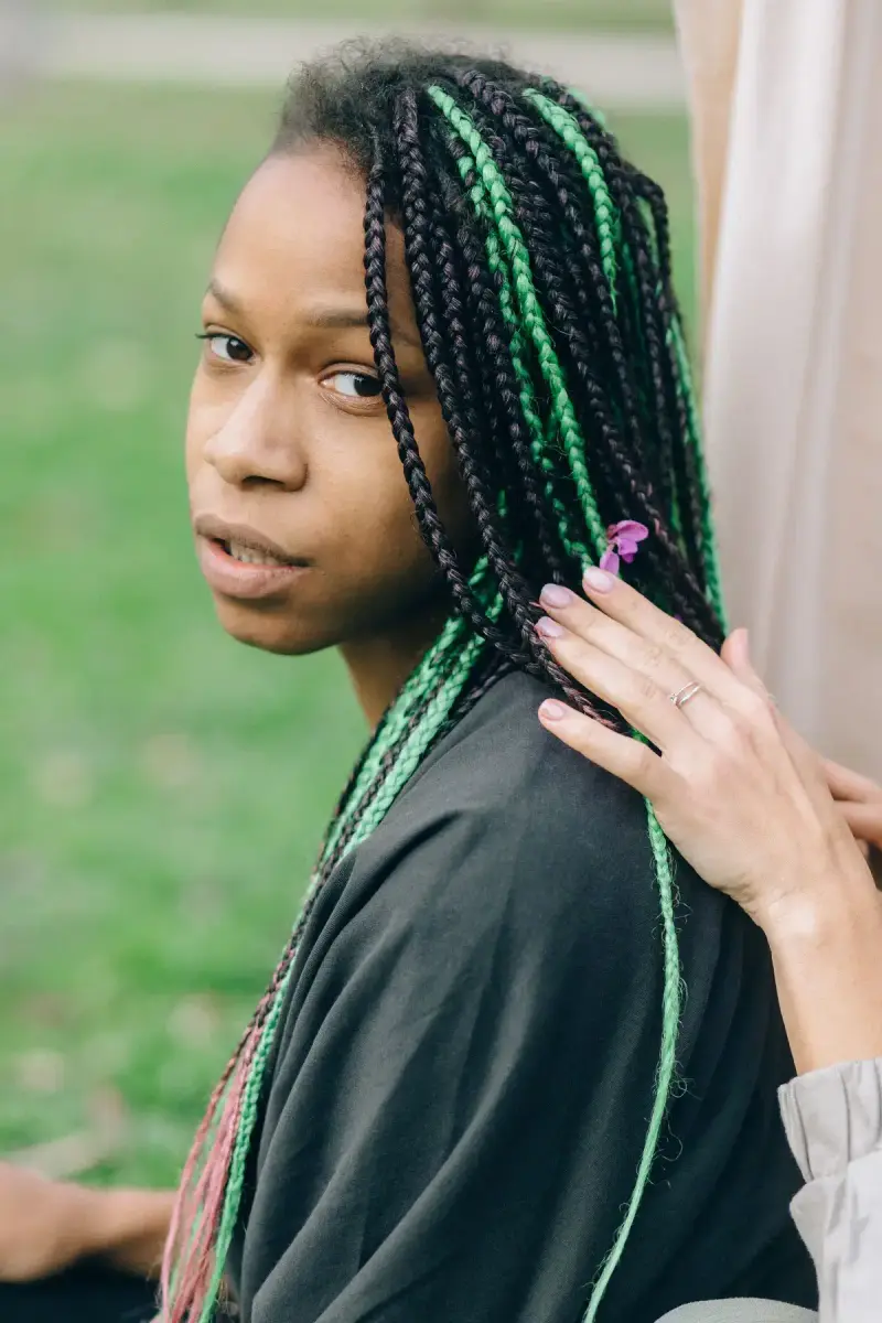 Woman with long box braids threaded in green and pink
