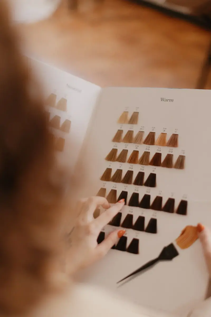 Hand choosing a shade from a hair color swatch book with a tint brush