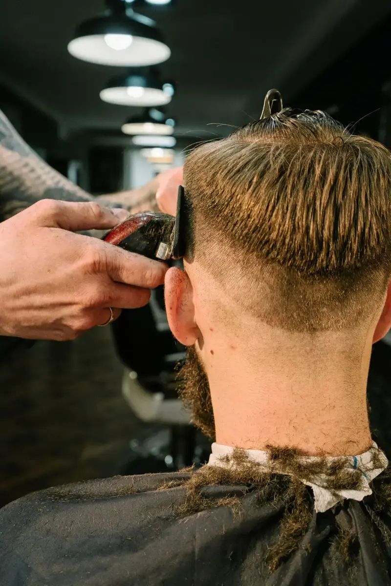 Barber clipper-cutting a man's hair in a barbershop with pendant lights