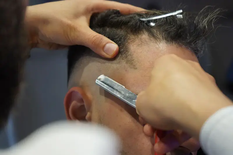 Barber using a straight razor to sharpen a fade on a client