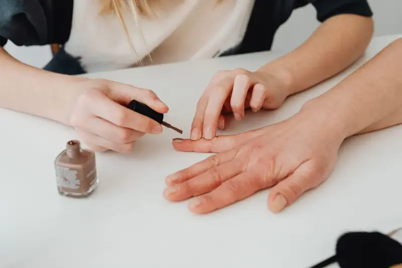 Hands of a nail technician applying polish during a salon manicure