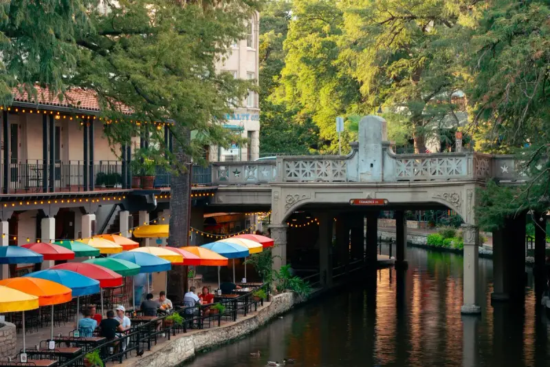 Outdoor dining along the San Antonio River Walk with greenery and a stone bridge