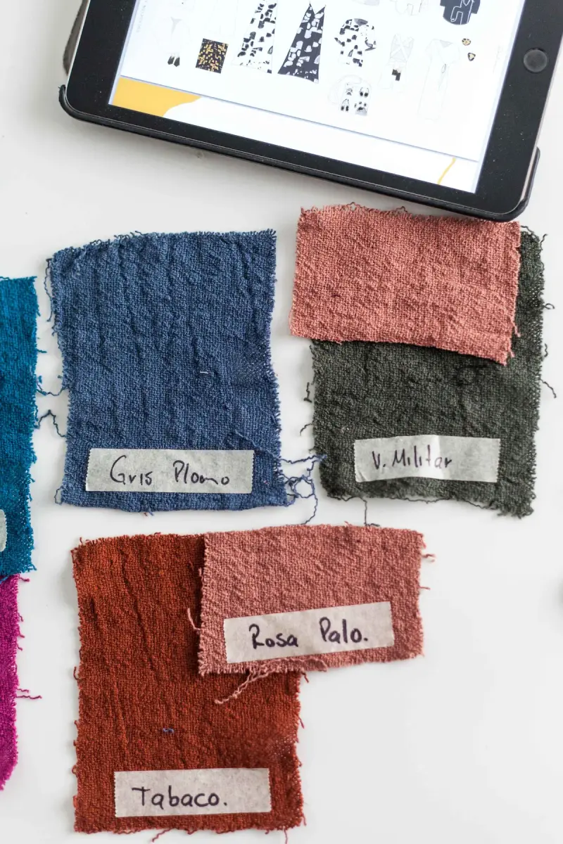 Textured fabric swatches with handwritten color labels beside a tablet