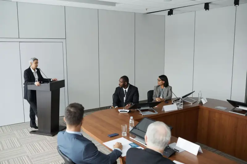 Speaker at a podium addressing colleagues seated at a horseshoe conference table