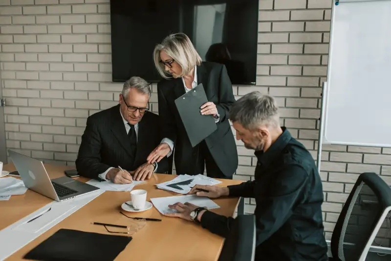 Senior professional signing documents while colleagues look on