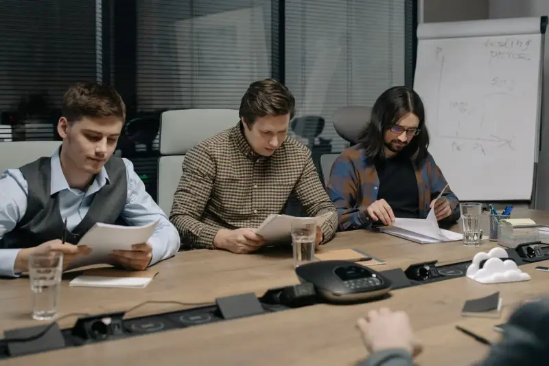 Three colleagues reviewing printed documents in a conference room