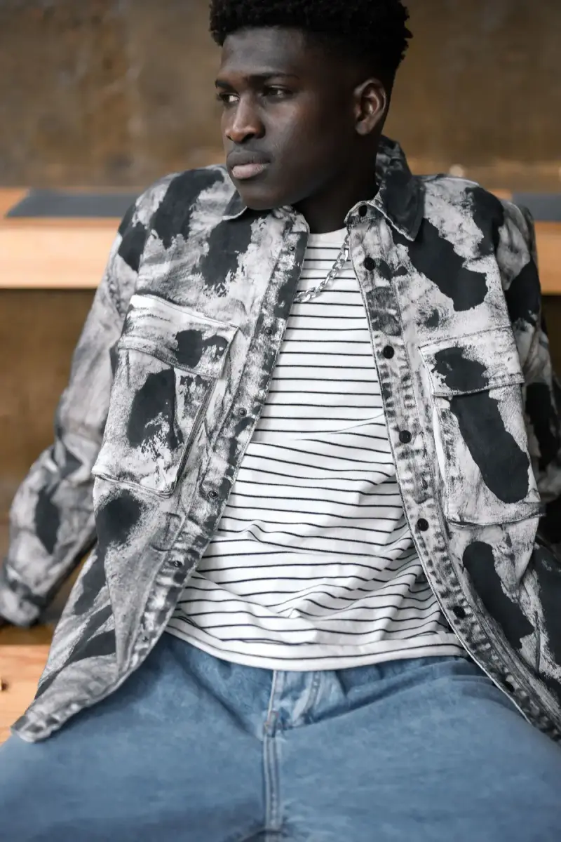 Man in a printed overshirt, striped tee and light jeans, seated close-up