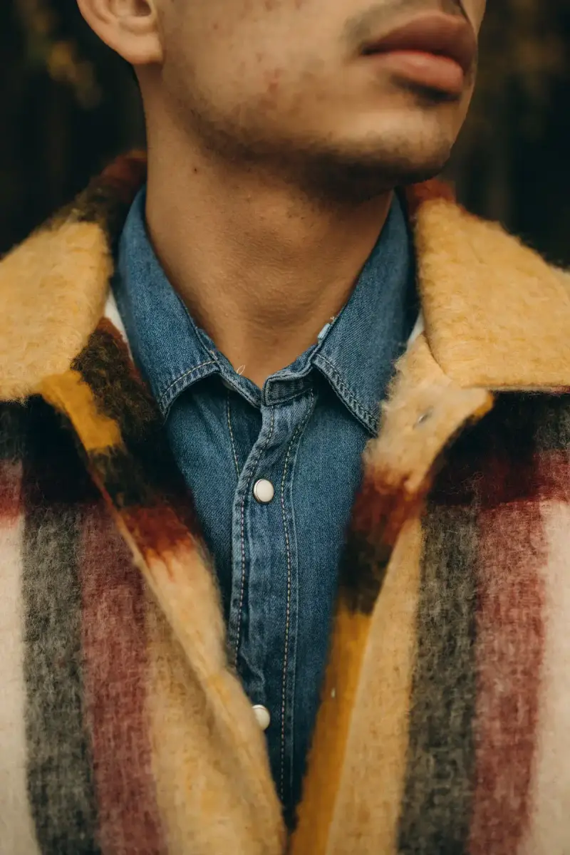 Close-up of a chambray shirt under a striped mohair coat on a young man