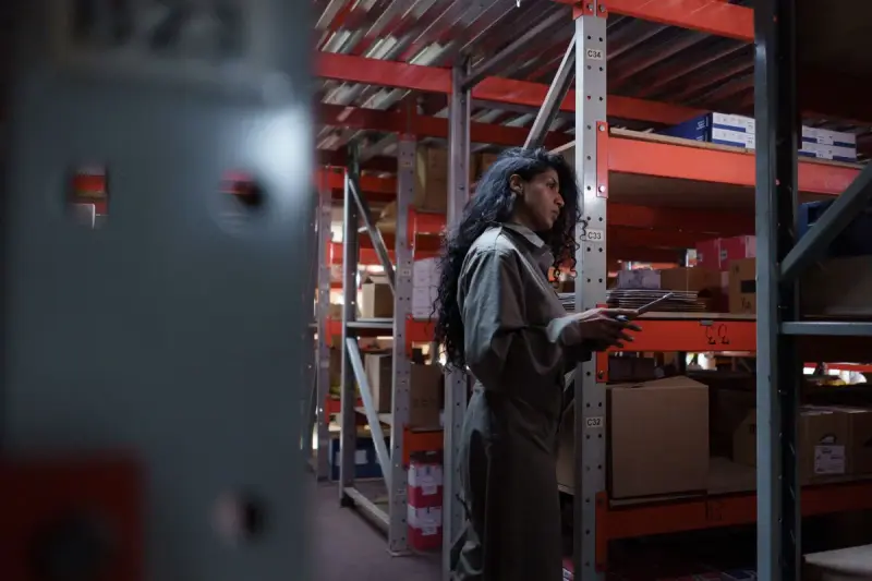 Woman in a grey uniform checking inventory in a warehouse aisle