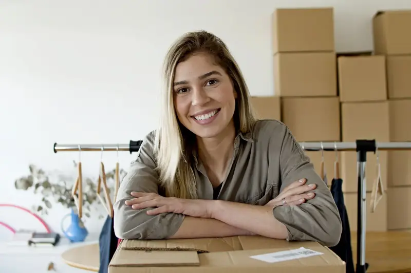 Smiling online store owner at her desk in front of stacked shipping boxes