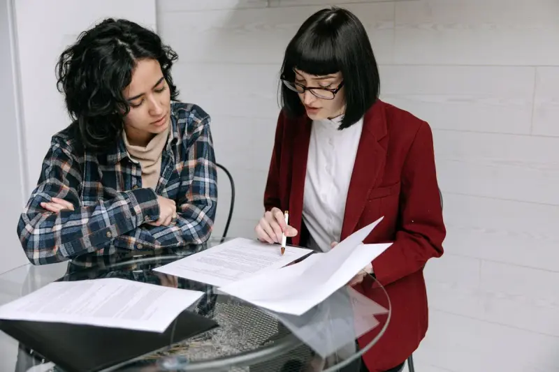 Two women reviewing business documents at a glass table