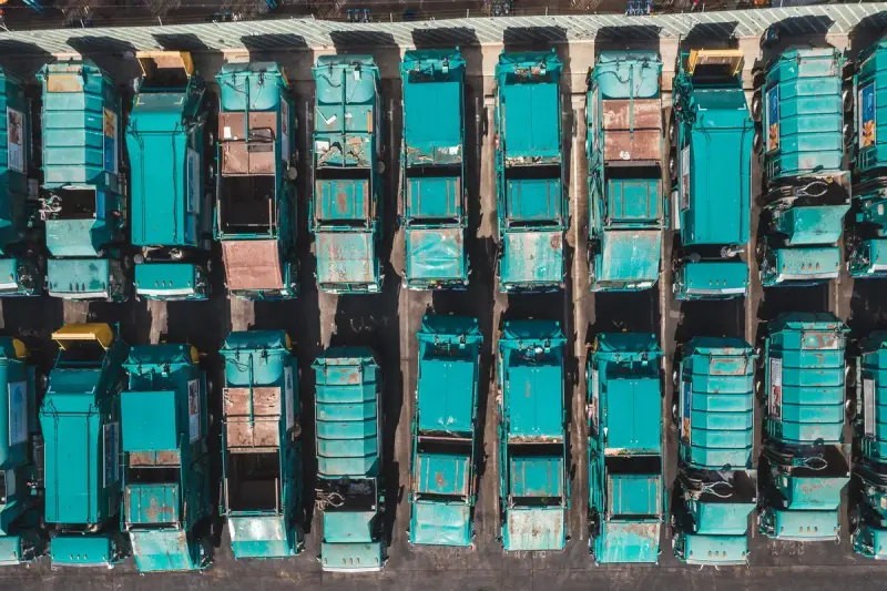 Aerial view of rows of turquoise garbage collection trucks parked side by side in a depot