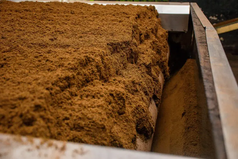 Close view of brown screened compost moving through a processing machine