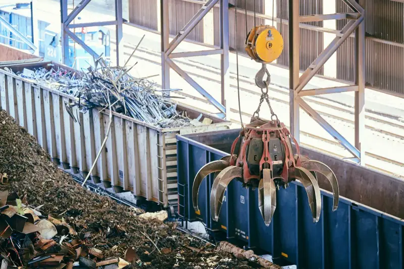 Orange grapple lifting scrap metal into a blue container at a recycling facility