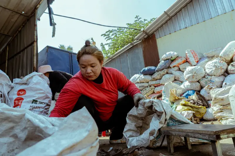 Woman in a red jacket sorting large sacks of recyclables outside a warehouse