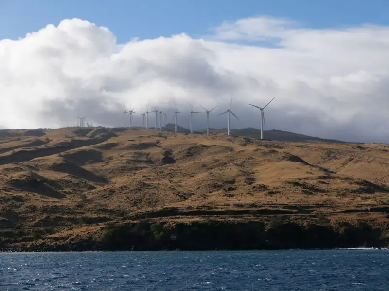 Row of wind turbines on a green hillside in Maui under clouds