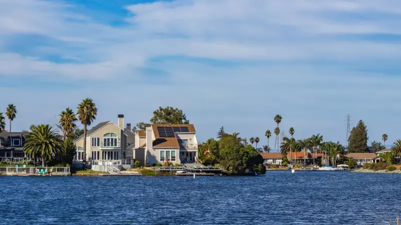 Waterfront homes with solar panels and palm trees reflected in blue water