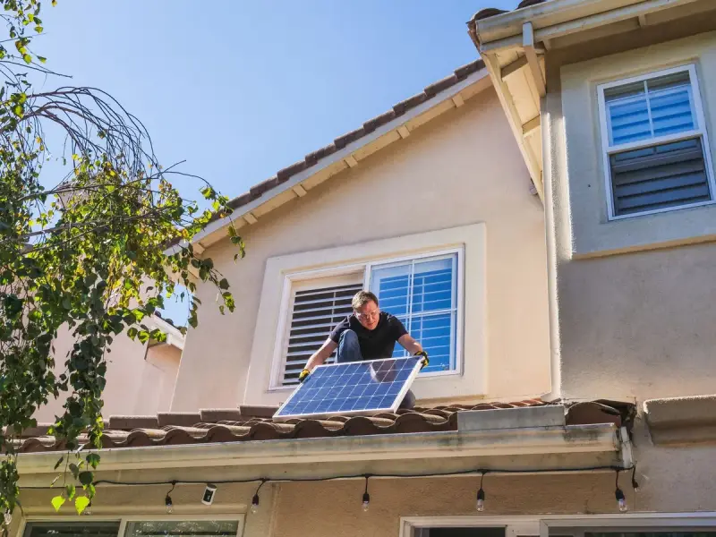 Technician setting a photovoltaic panel on a tiled house roof under blue sky