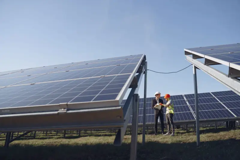 Supervisor in a hardhat reviewing plans with a technician beside solar panels