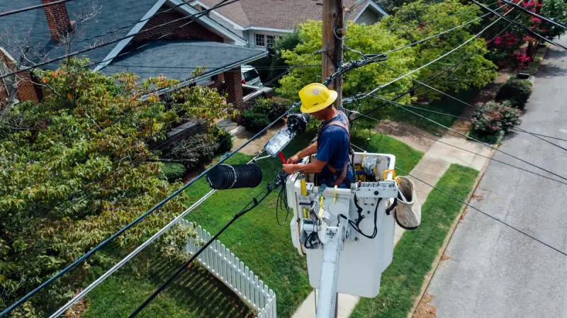 Line worker in a bucket lift repairing power lines above a residential street