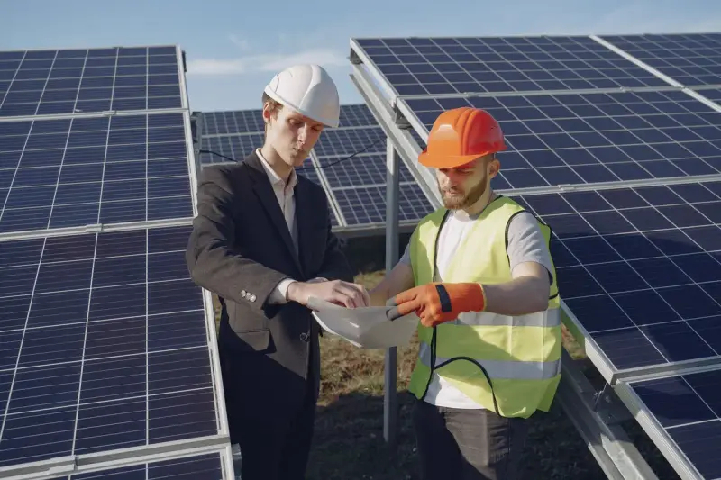 Project manager and foreman in hardhats checking documents between solar panels