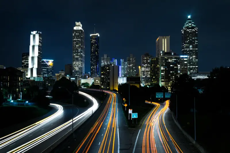 Downtown Atlanta towers lit at night above light trails on Freedom Parkway, seen from Jackson Street Bridge