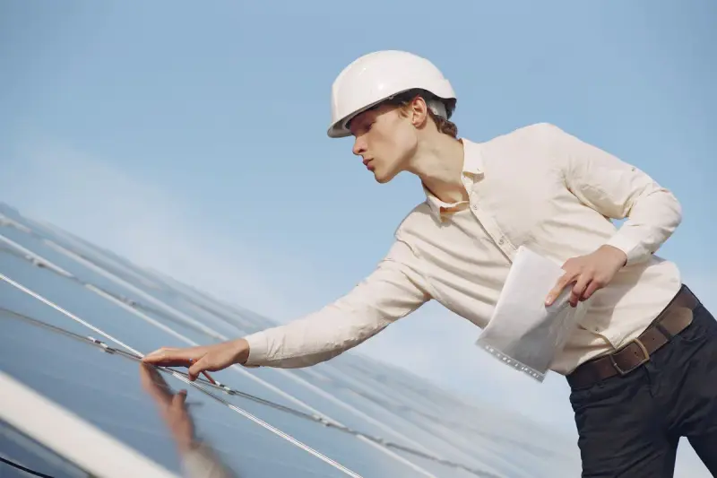 Solar technician in a hard hat inspecting photovoltaic panels in the sun