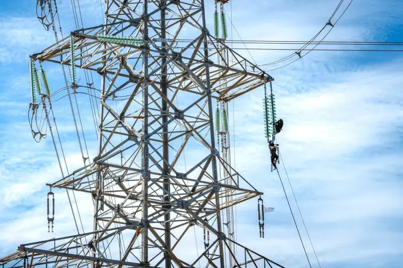 Line workers performing maintenance high on a transmission line against a blue sky