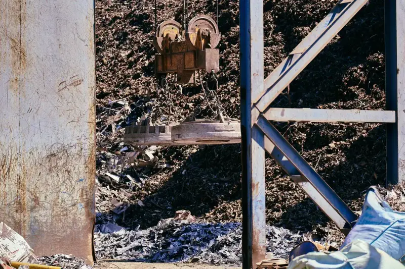 Lifting magnet on a crane hanging over a pile of shredded steel scrap in daylight