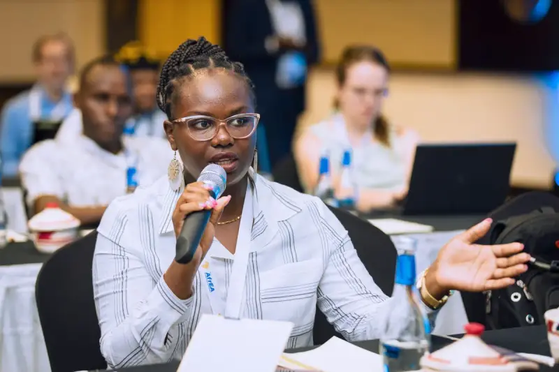 Woman speaking into a microphone during a conference session with attendees behind her