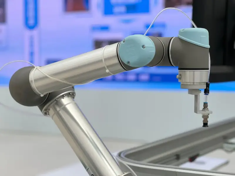 Close-up of a silver collaborative robot arm with a suction gripper reaching over a work tray