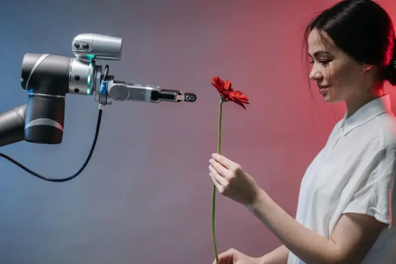 Smiling woman taking a red flower handed to her by a collaborative robot arm