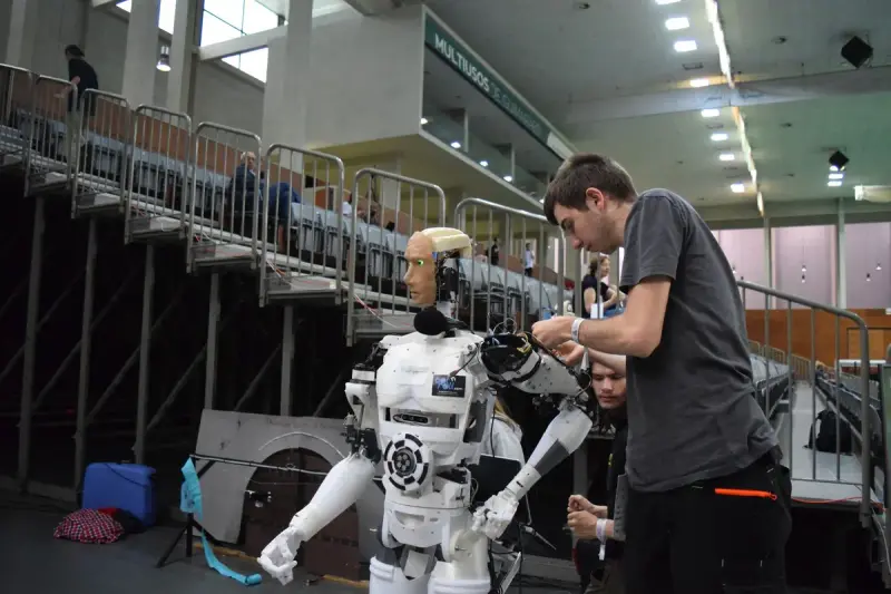 Technician adjusting the arm of a white humanoid robot in an exhibition hall