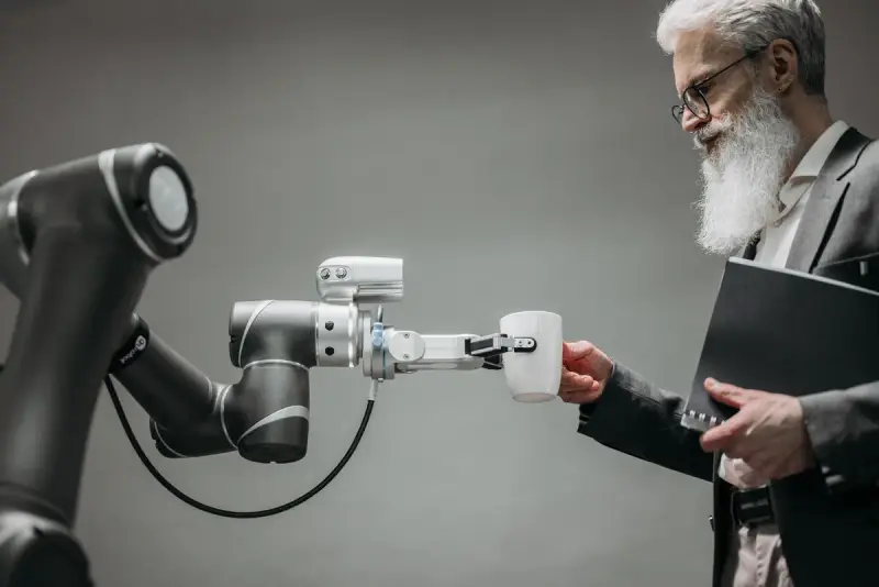 Bearded man in a suit taking a cup from the gripper of a collaborative robot arm