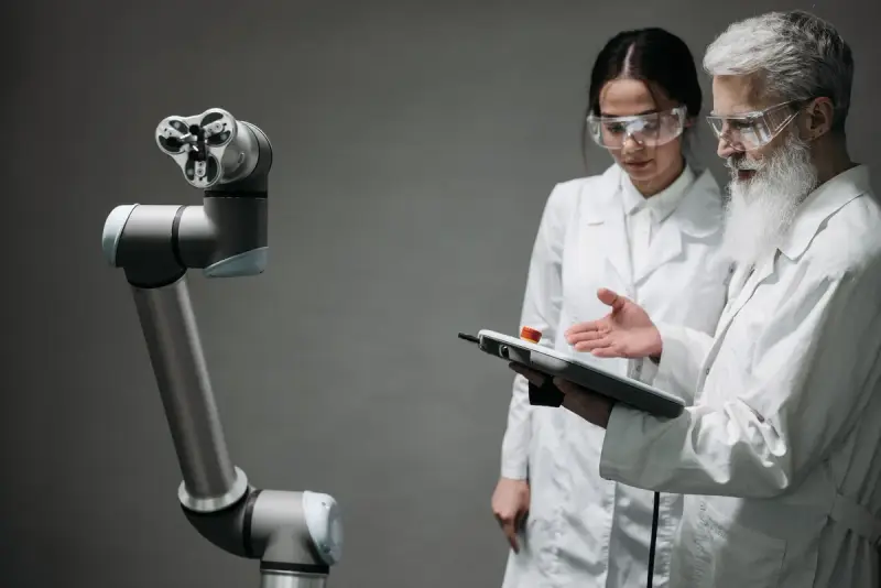 Two researchers in lab coats reviewing a tablet beside a collaborative robot arm