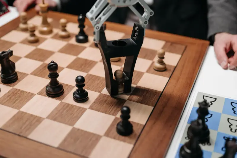 Robot gripper picking up a chess pawn from a wooden chessboard