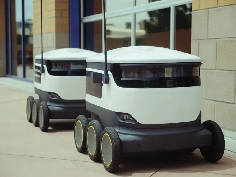 Two six-wheeled autonomous delivery robots parked beside a building