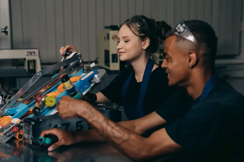 Young woman and man smiling while building a wheeled robot in a workshop