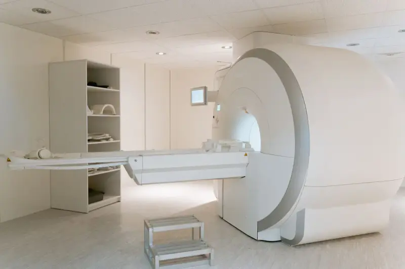 Empty MRI scanner room with the patient table extended and storage shelves on the wall