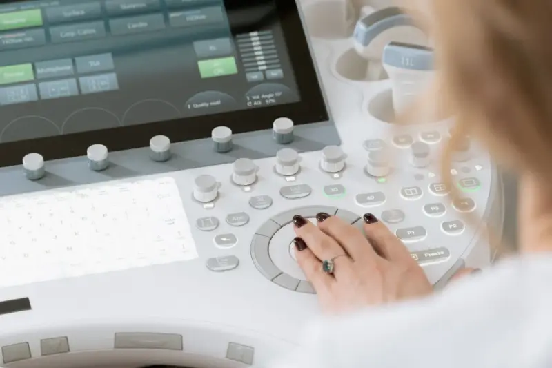 A woman's hand on the trackball and controls of an ultrasound console