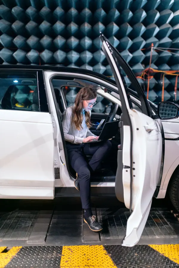 An automotive engineer works with a laptop during acoustic testing in an anechoic chamber photograph.
