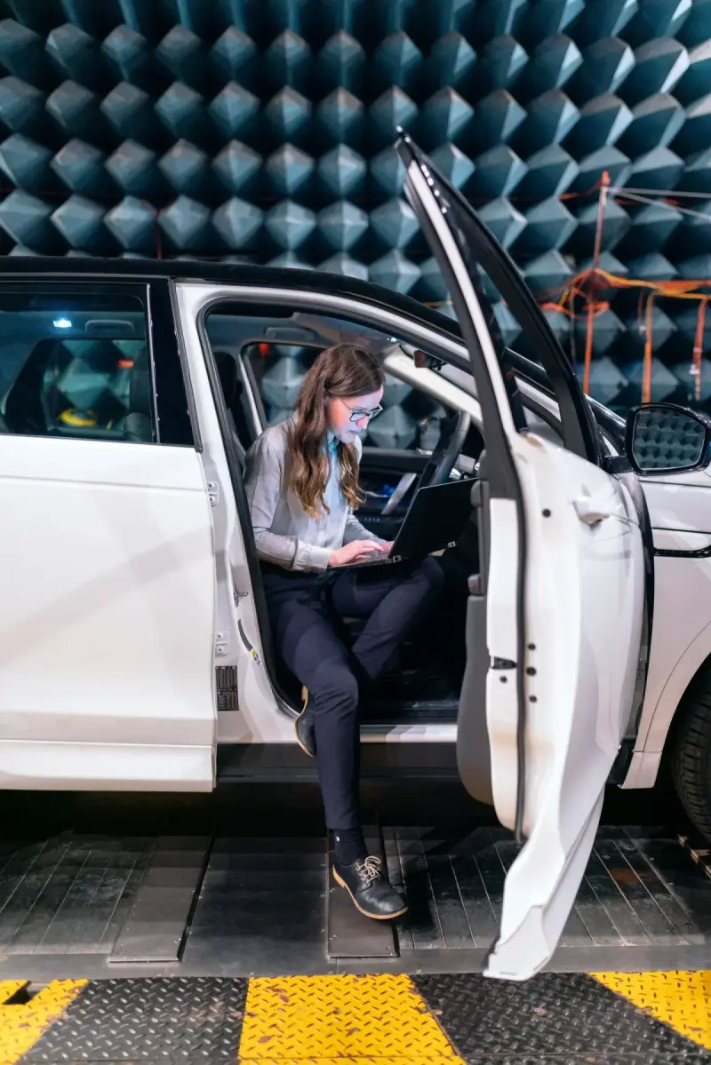 An automotive engineer works with a laptop during acoustic testing in an anechoic chamber photograph.