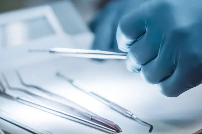 Gloved hand of a surgeon holding steel surgical instruments