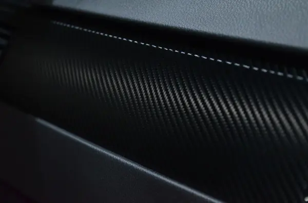 Close view of a dark carbon-fiber-patterned automotive surface.